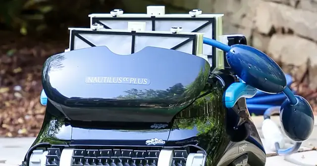 Dolphin Nautilus CC Plus robotic pool cleaner on a stone pool deck with its filter lid open and the floating cable coiled beside it
